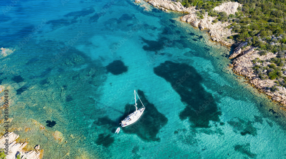 View from above, stunning aerial view of a sailboat floating on a beautiful turquoise sea that bathes the green and rocky coasts of Sardinia. Emerald Coast (Costa Smeralda) Italy