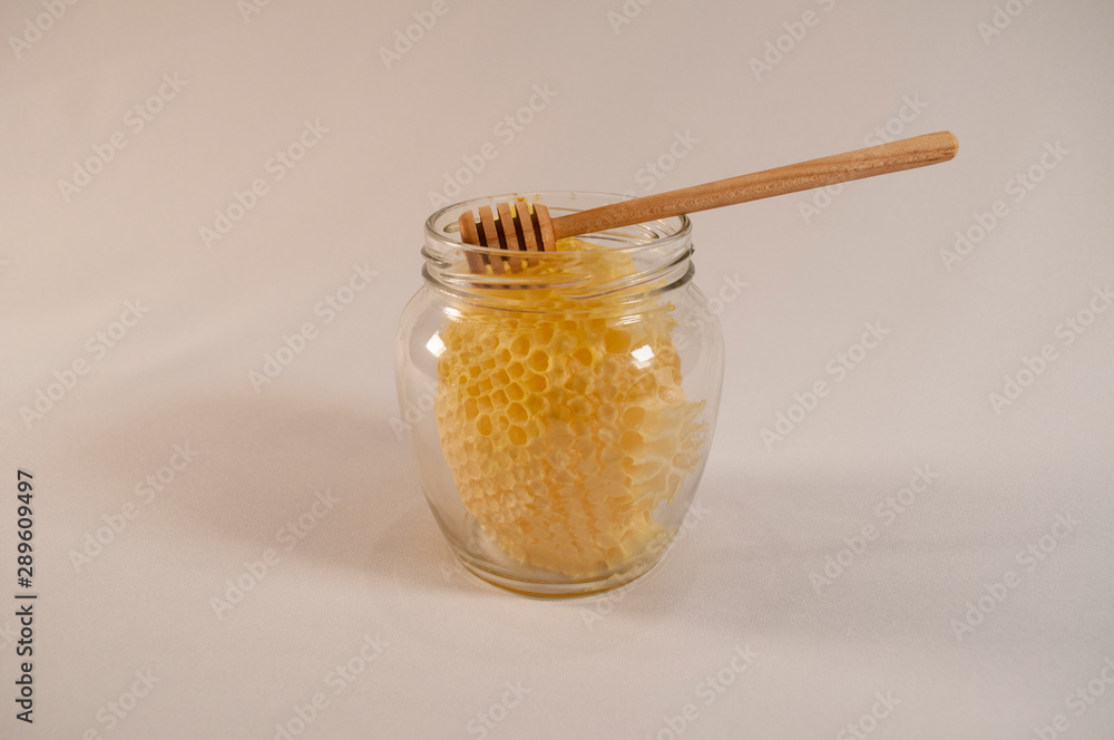Frame with sealed honey, a glass jar with golden honey and a wooden spoon for mixing and tasting natural honey Frame with sealed honey, a glass jar with golden honey and a wooden spoon for mixing and tasting natural honey