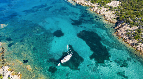 View from above  stunning aerial view of a sailboat floating on a beautiful turquoise sea that bathes the green and rocky coasts of Sardinia. Emerald Coast  Costa Smeralda  Italy