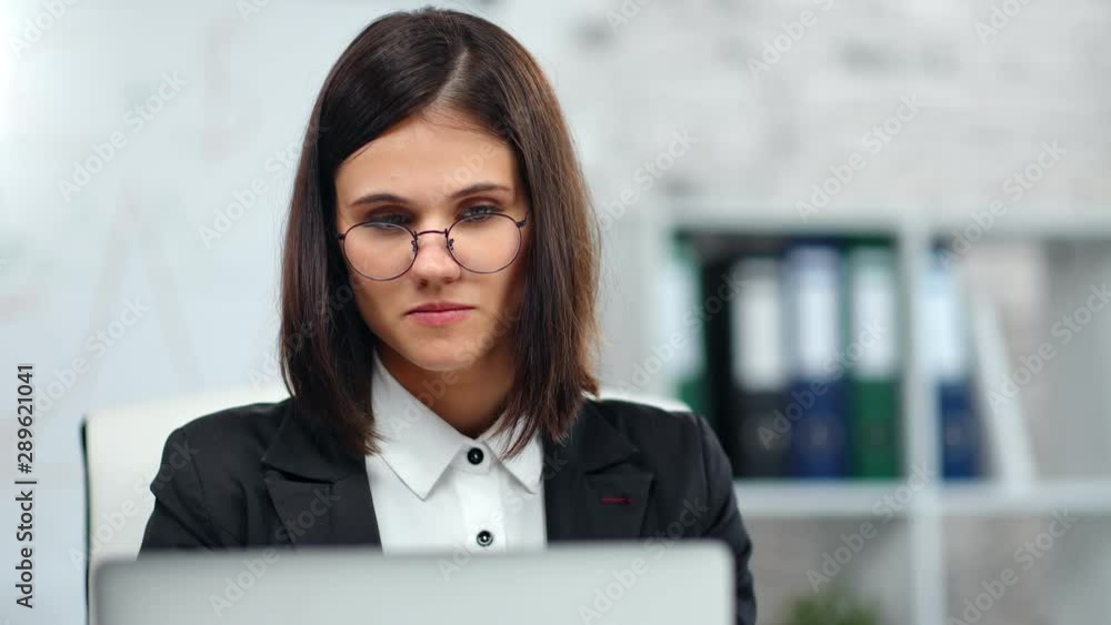 Beautiful pensive female office worker bookkeeper looking at screen of computer at white workplace Beautiful pensive female office worker bookkeeper looking at screen of computer at white workplace