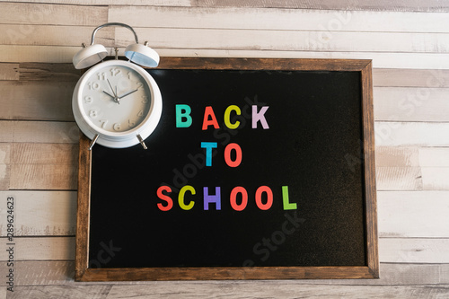 Blackboard with text back to school and an alarm clock