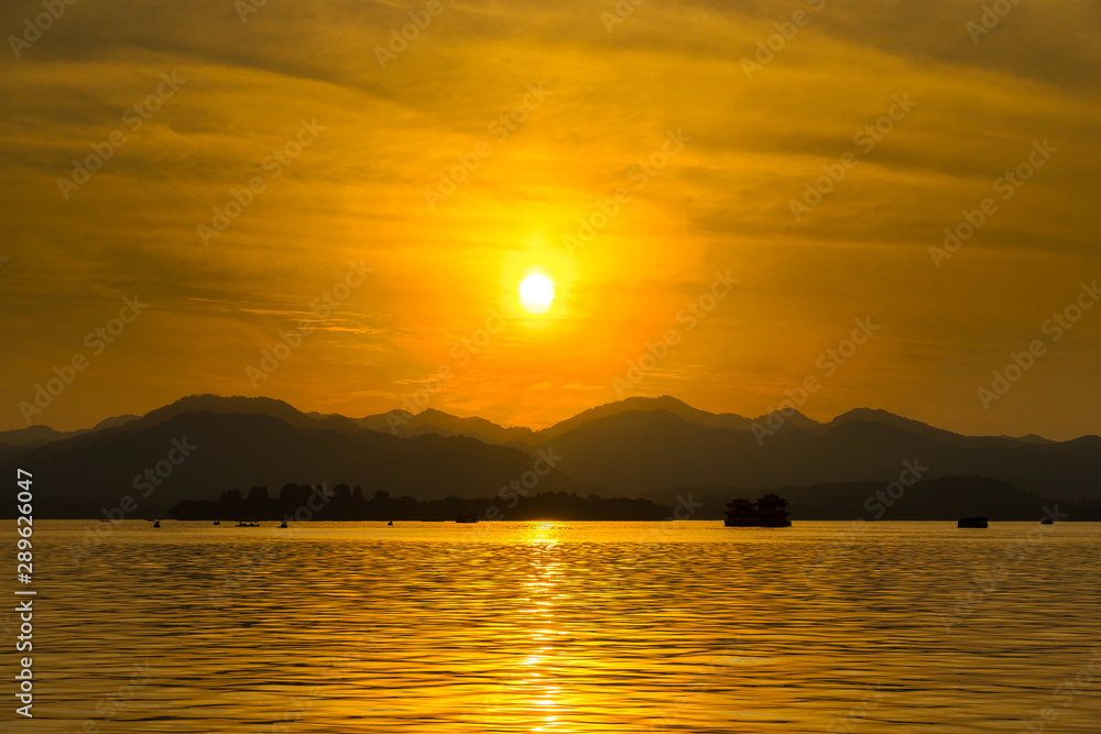 Naklejka premium The landscape Background of a golden sunset reflect water and silhouette mountain in west lake (xihu) in Hangzhou CHINA - Image