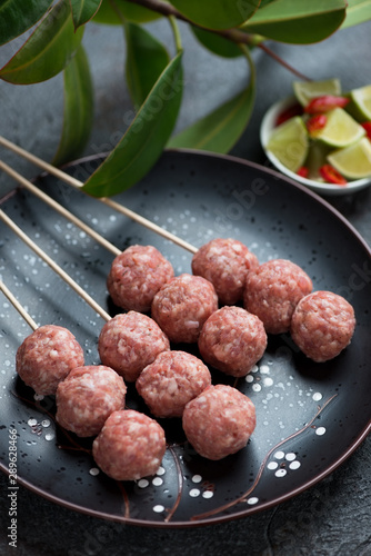 Fresh uncooked nem nuong or vietnamese pork meatballs on skewers, vertical shot, closeup