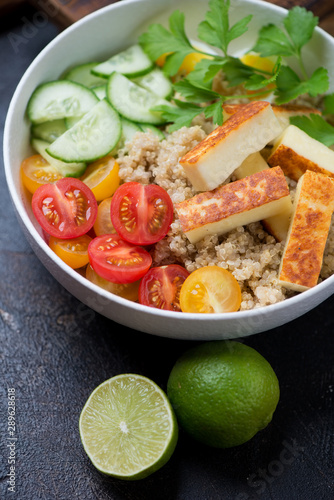 Quinoa, roasted cheese, cherry tomatoes, cucumber and parsley in a bowl, close-up on a dark brown stone surface