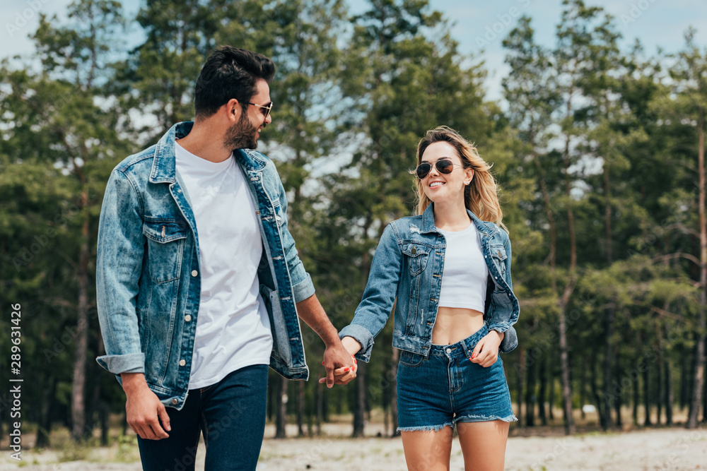 attractive woman and handsome man in denim jackets smiling and holding hands attractive woman and handsome man in denim jackets smiling and holding hands