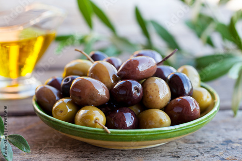 Assortment of fresh olives on a plate with olive tree brunches. Wooden background.
