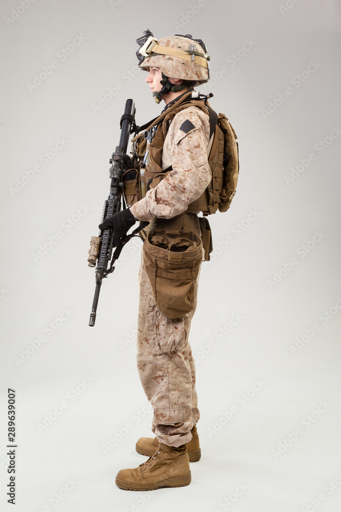 Soldier in US marines uniform with rifle on light grey background, studio shot Soldier in US marines uniform with rifle on light grey background, studio shot