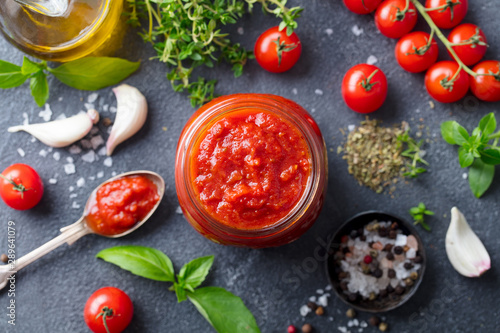 Tomato sauce in a glass jar with fresh herbs, tomatoes and olive oil. Top view. Slate background.