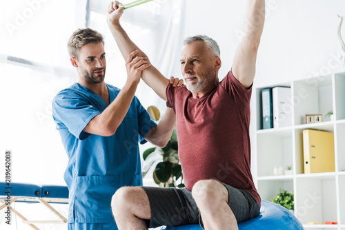 doctor near middle aged man exercising with resistance band