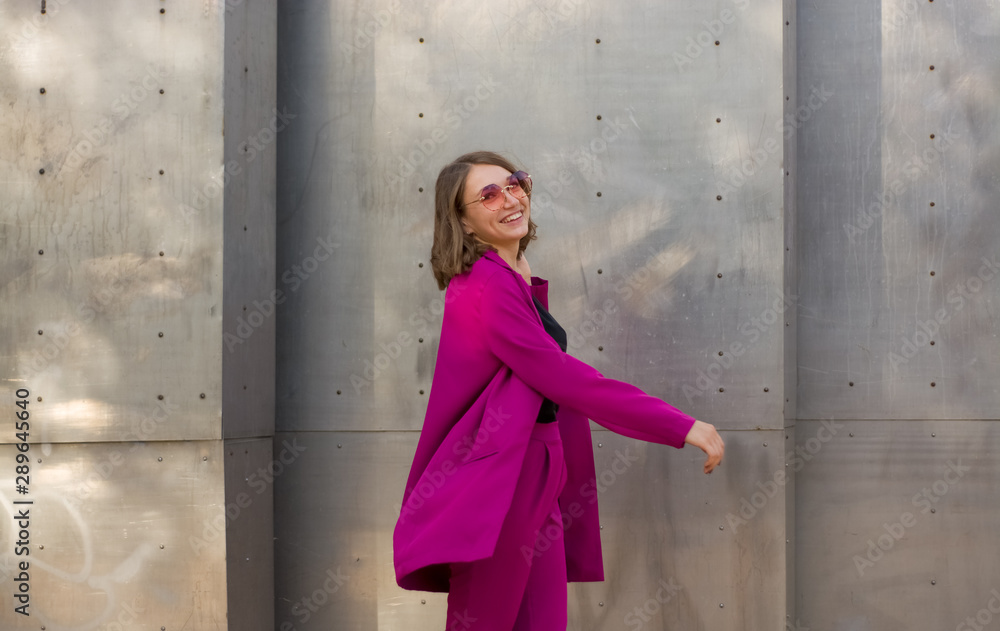 A girl in trendy plum and bright suit walks around the city and has fun. Style.