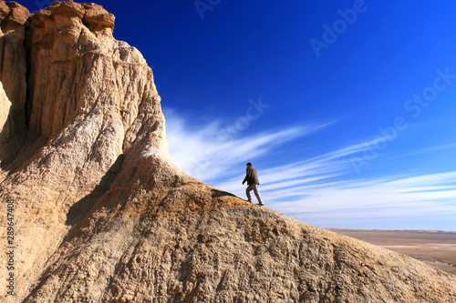 Unrecognisable man climbing a beautifully coloured hill with exploding like cloud movement in Tsagaan Suvraga « white stupa » in the Gobi desert, Mongolia.