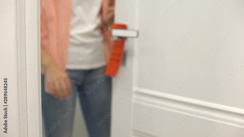Woman hanging sign on doorknob Do not disturb, hotel rules of client privacy Woman hanging sign on doorknob Do not disturb, hotel rules of client privacy