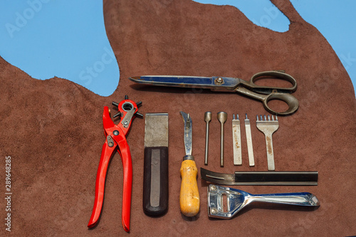Rusty leather craft tools on a leather background. Leather craftmans work desk . Piece of hide and working handmade tools on a work table.