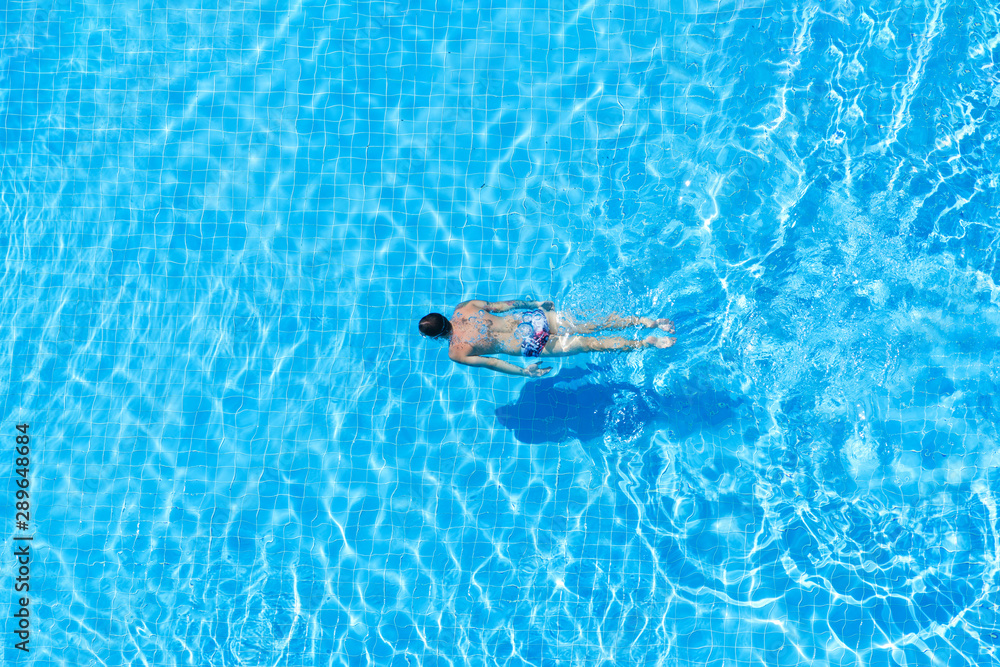 Top view of a man swimming underwater in a pool.