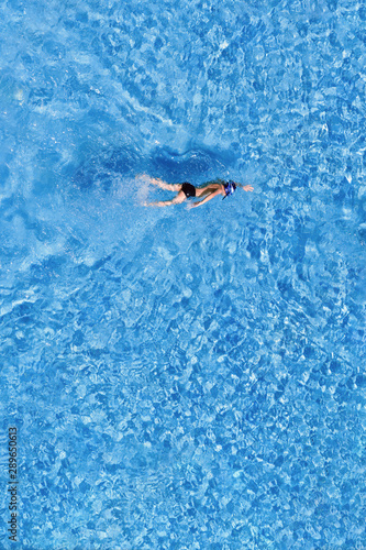 Top view of a boy swimming in a pool in a hat outdoors.