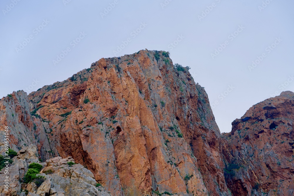 Red-brown cliff under a light blue sky
