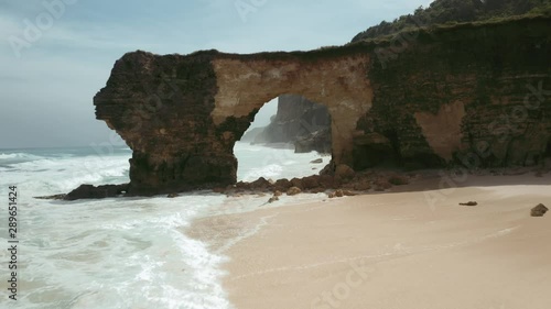 Backward low drone shot of Bawana Beach, through the rock tunnel in front of the ocean photo