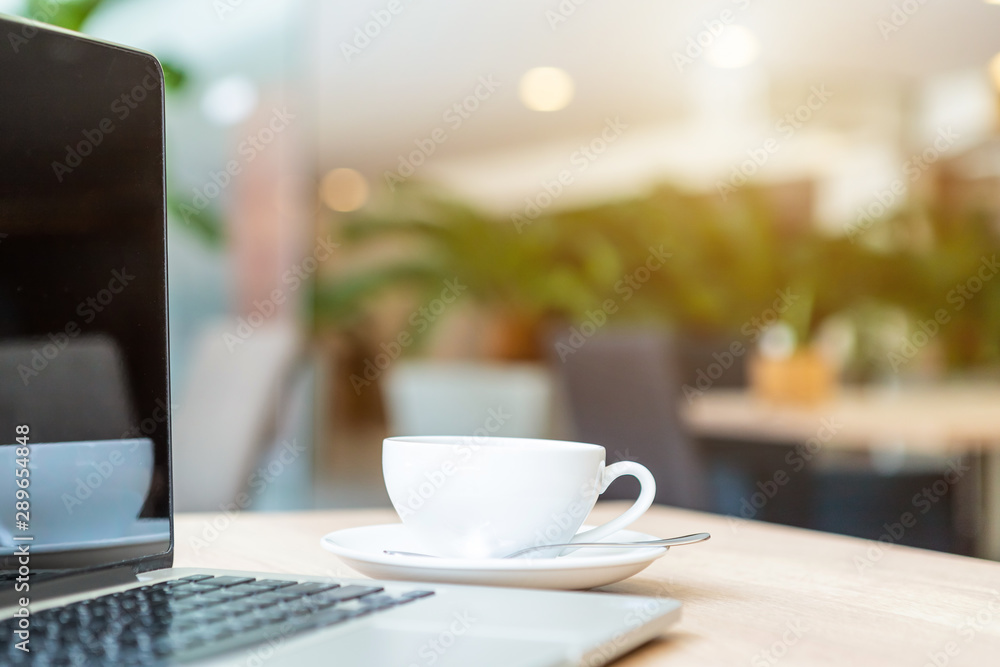Close-up of Business laptop computer and coffee cup on wooden table of In the coffee shop background Close-up of Business laptop computer and coffee cup on wooden table of In the coffee shop background