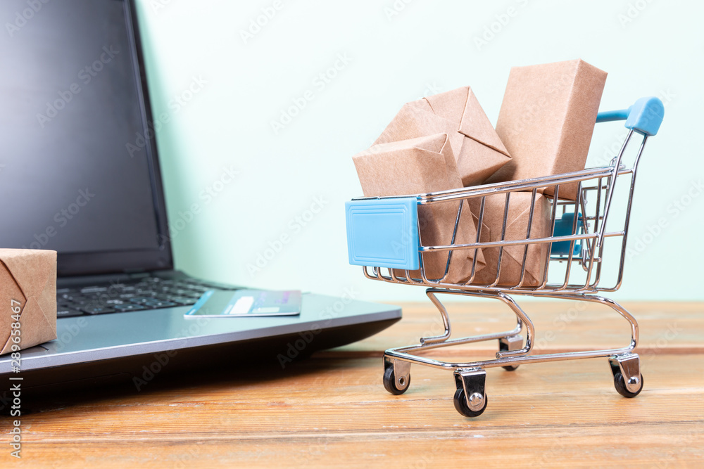 Online shopping concept. Shopping cart, small boxes, laptop and credit card on the desk Online shopping concept. Shopping cart, small boxes, laptop and credit card on the desk