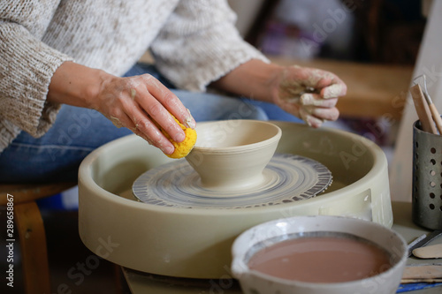 woman shapes clay cup with tools on potter's wheel