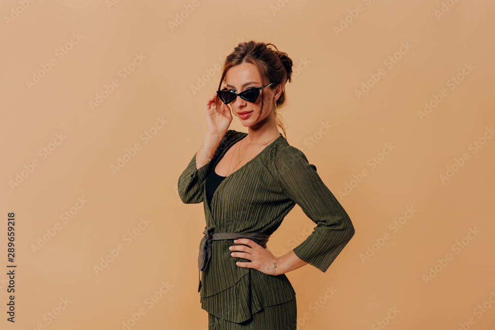 Studio portrait of attractive fashionable woman wearing suit and sunglasses posing over isolated background 