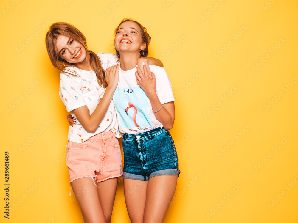 Two young beautiful smiling hipster girls in trendy summer clothes. Sexy carefree women posing near yellow wall in studio. Positive models going crazy and having fun.Hugging Two young beautiful smiling hipster girls in trendy summer clothes. Sexy carefree women posing near yellow wall in studio. Positive models going crazy and having fun.Hugging