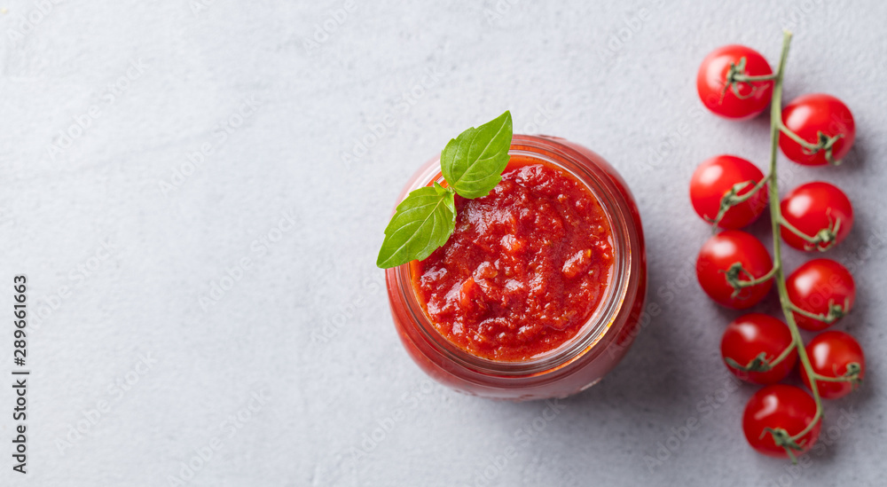 Tomato sauce with basil in a glass jar with fresh tomatoes. Grey background. Top view. Copy space. - obrazy, fototapety, plakaty 
