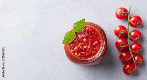 Tomato sauce with basil in a glass jar with fresh tomatoes. Grey background. Top view. Copy space.
