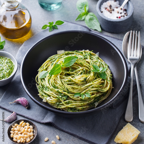 Pasta spaghetti with pesto sauce and fresh basil leaves in black bowl. Grey background.