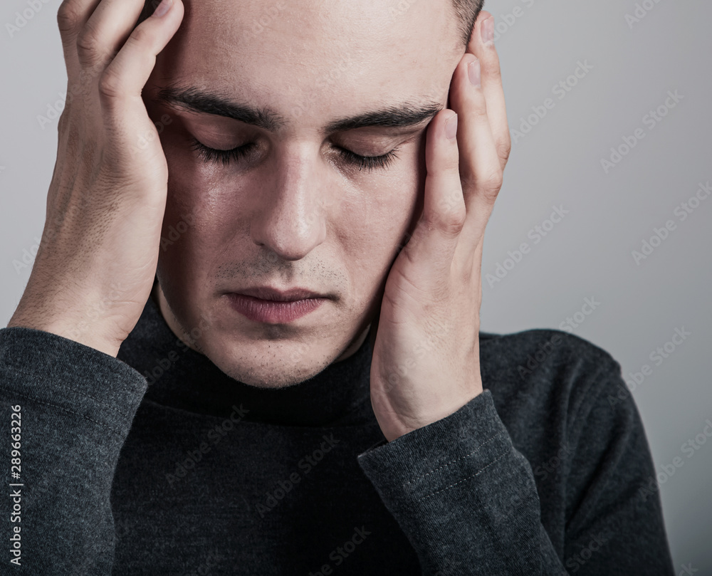 Unhappy crying ill man with headache holding the head. Closeup studio portrait on grey background. Negative problem concept. Unhappy crying ill man with headache holding the head. Closeup studio portrait on grey background. Negative problem concept.