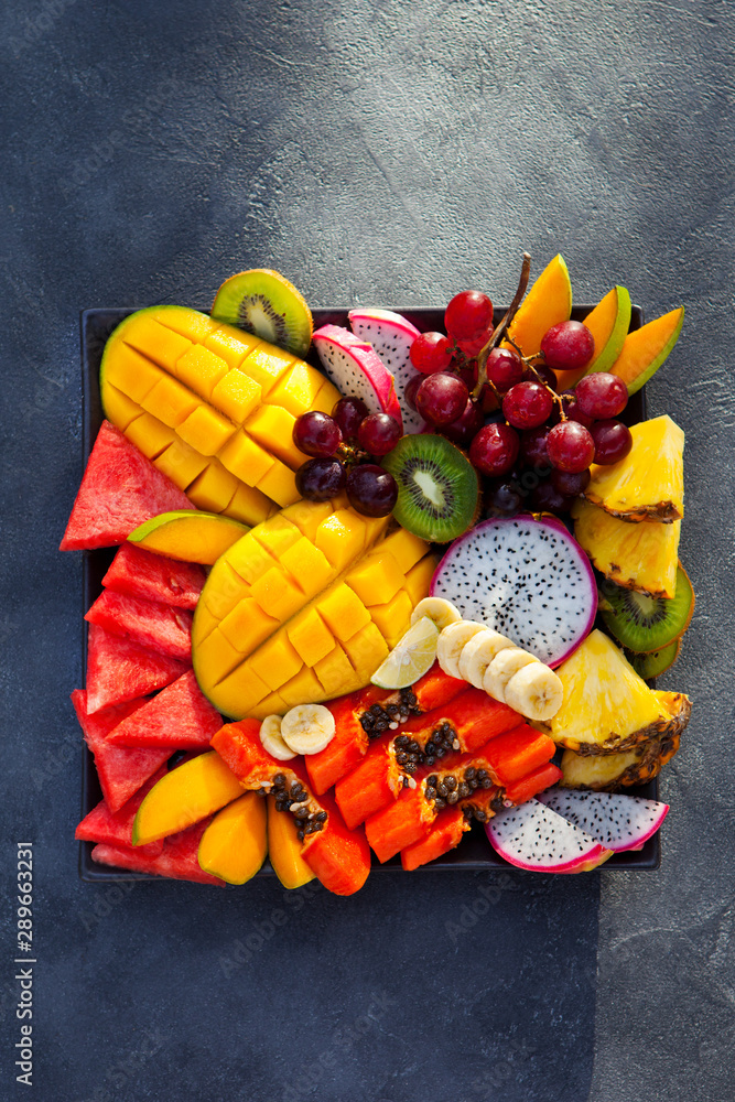 Tropical fruits assortment on a plate. Slate background. Copy space. Top view.