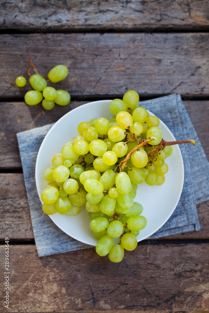 Green grape on a white plate. Grey wooden background. Top view. Copy space. Green grape on a white plate. Grey wooden background. Top view. Copy space.