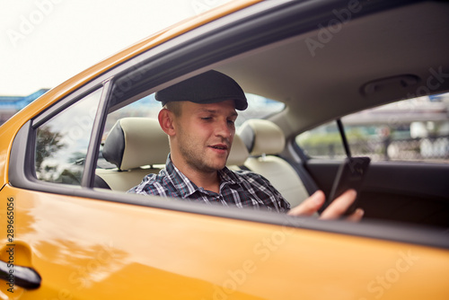 Photo of young man in cap with phone in hand sitting in yellow car © snedorez