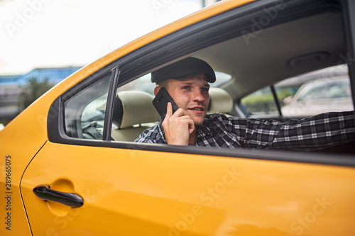 Image of man in cap with phone in hand sitting in back seat in yellow car © snedorez
