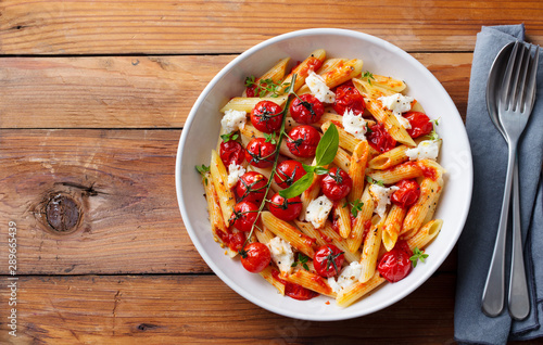 Pasta penne with roasted tomato, sauce, mozzarella cheese and fresh basil. Top view. Copy space. Wooden background.