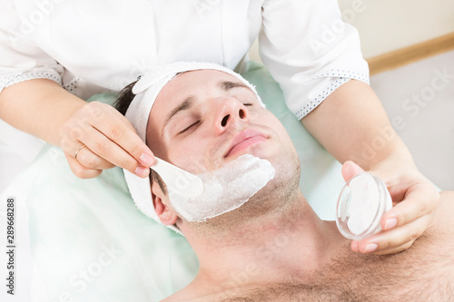 Cosmetic procedure for applying a therapeutic mask to a young man in a beauty salon.