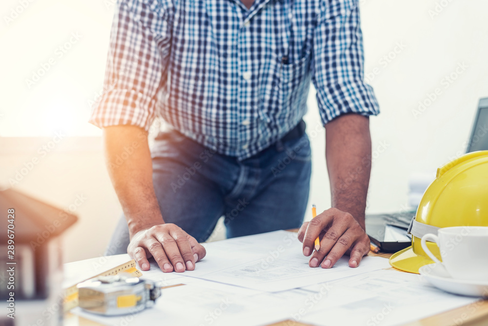 Asian architect man Standing working with blueprints sketching a construction project on wood desk at home office.Construction design concept. Asian architect man Standing working with blueprints sketching a construction project on wood desk at home office.Construction design concept.