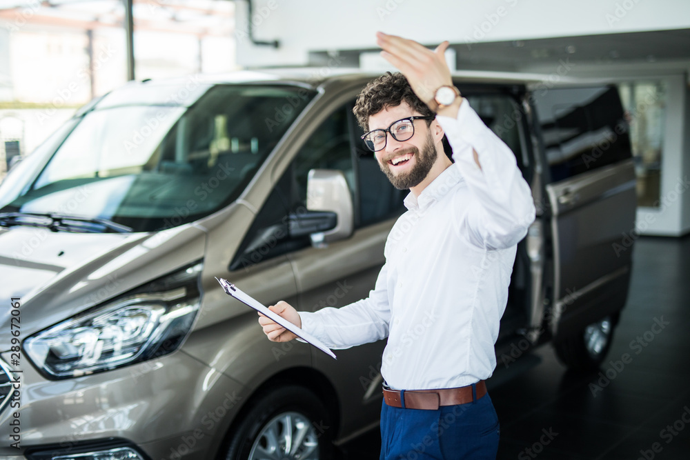 Handsome car dealership worker smiling while standing near the car
