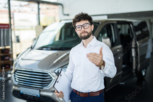 Confident young car dealer standing in showroom and welcome clients. © F8  \ Suport Ukraine