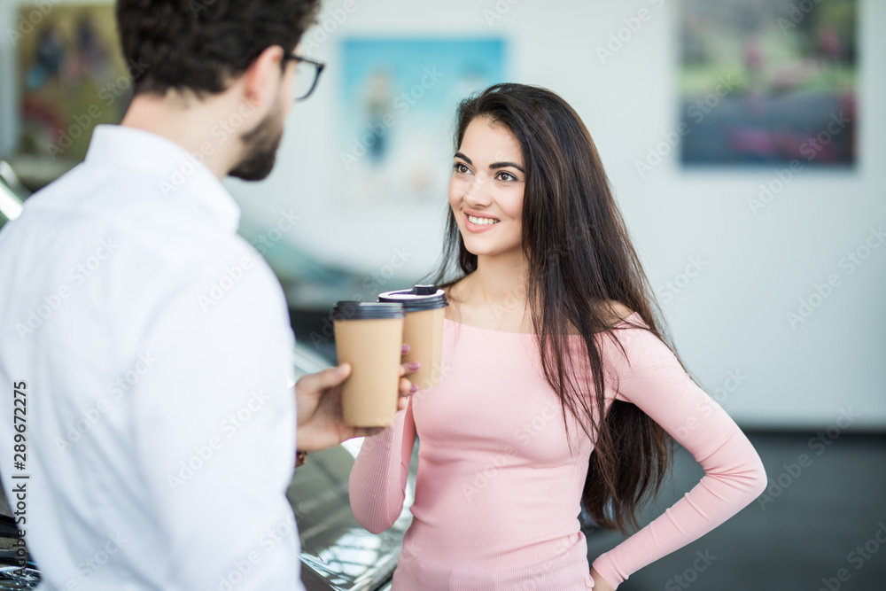 Dealer speaking with a client in a dealership while drinking coffee and discuss car purchase Dealer speaking with a client in a dealership while drinking coffee and discuss car purchase