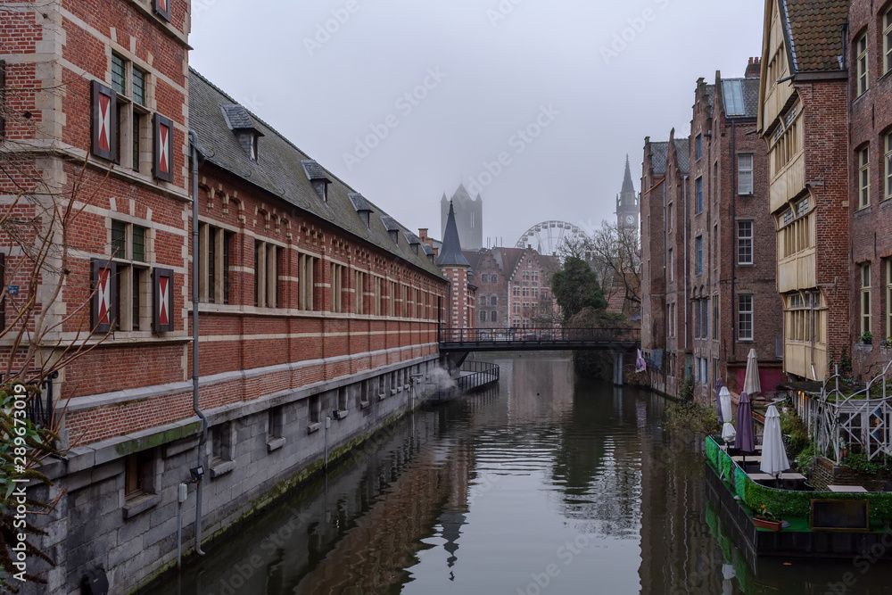 Picturesque old street of Ghent with traditional medieval houses, canal, bridge, ferris wheel and towers. Cityscape of Ghent street.