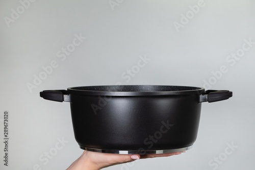Closeup side view of empty new black modern saucepan in hands of white woman ready to use cooker for cooking tasty home food. Horizontal color photography.