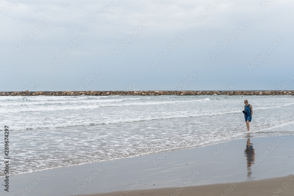 Lonely woman walking pensively by the sea shore on the beach
