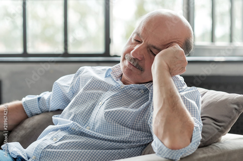 Schilderij op canvas Tired senior hispanic man sleeping on couch, taking afternoon nap at the living