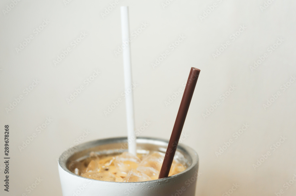 Brown and white straw in iced coffee. Stainless steel cup Brown and white straw in iced coffee. Stainless steel cup
