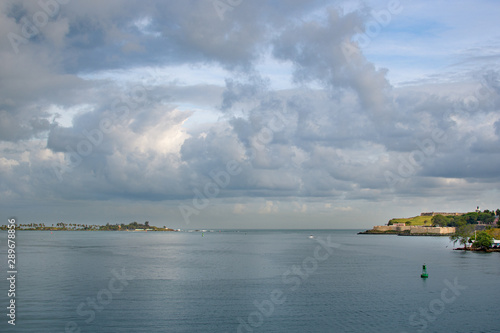 View of San Juan Bay and Fort San Felipe del Morro in pre-storm weather. Dense thunderclouds and sunbeams are reflected in the sea.