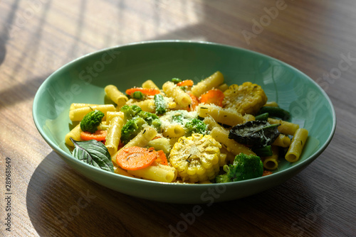 Delicious fresh warm paste sprinkled with cheese parmesan with broccoli, corn, carrots and other vegetables. Vegetarian food