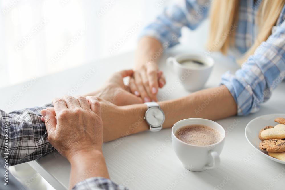 Fototapeta premium Daughter and mother holding hands while drinking hot coffee at table