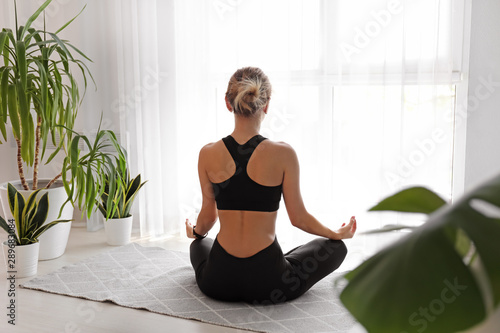 Young woman meditating at home, back view