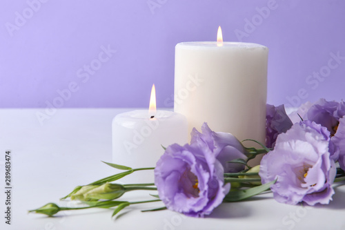 Burning candles with fresh flowers on table against color background